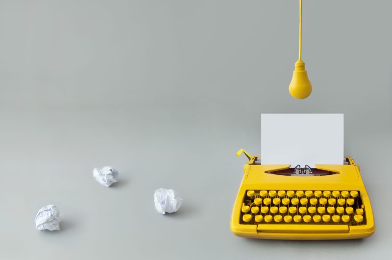 Retro typewriter with crumpled pieces of paper and yellow hanging light bulb